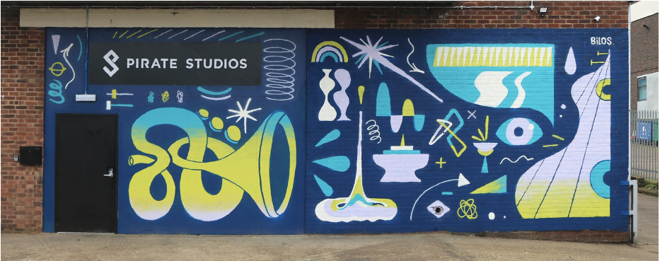  graffiti in blue and yellow over the brick and a black security door with black sign above it saying pirate studios in white