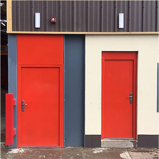 Outside shot of a factory with two orange steel doors next to each other one with a infill panel above also orange